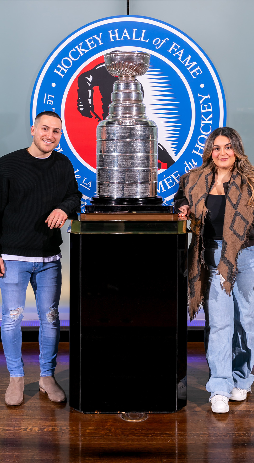 Couple stand on either side of the Stanley Cup in the Great Hall at the Hockey Hall of Fame